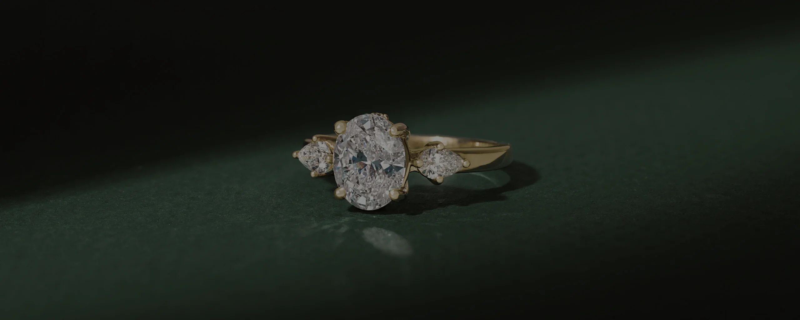 A three-stone diamond ring illuminated against deep green