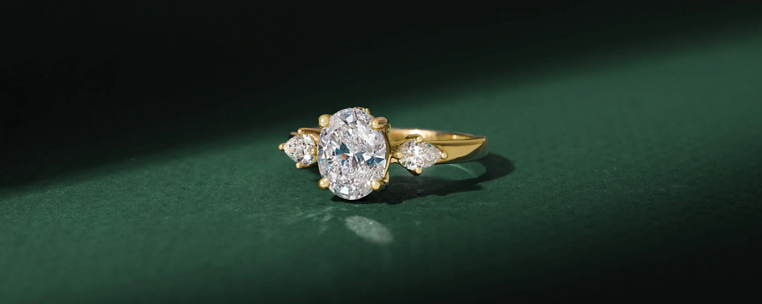 A three-stone diamond ring illuminated against deep green